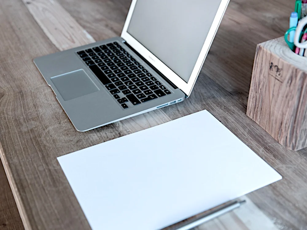 Laptop, Notizblock und Stift auf aufgeräumtem Tisch als Symbol für digitale Ordnung in der Familie