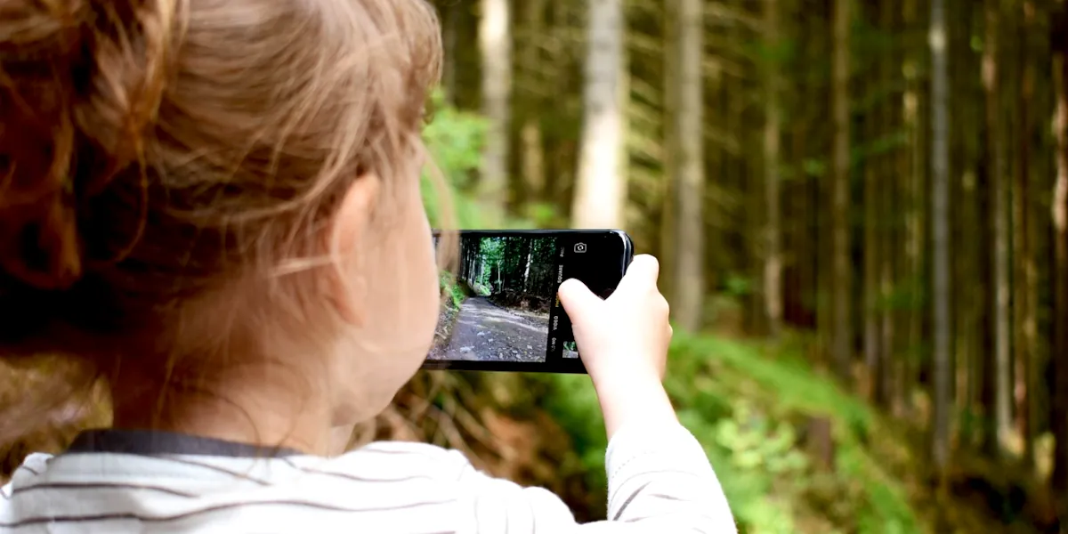 Kind fotografiert mit einem Smartphone im Wald – Familienfotos sicher speichern